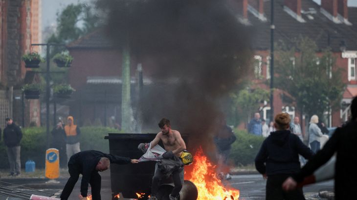 Rellen in Belfast na mesaanval: auto’s en gebouwen in brand gestoken Rellen in Belfast na mesaanval: auto's en gebouwen in brand gestoken (Picture by: aljazeera.com)
